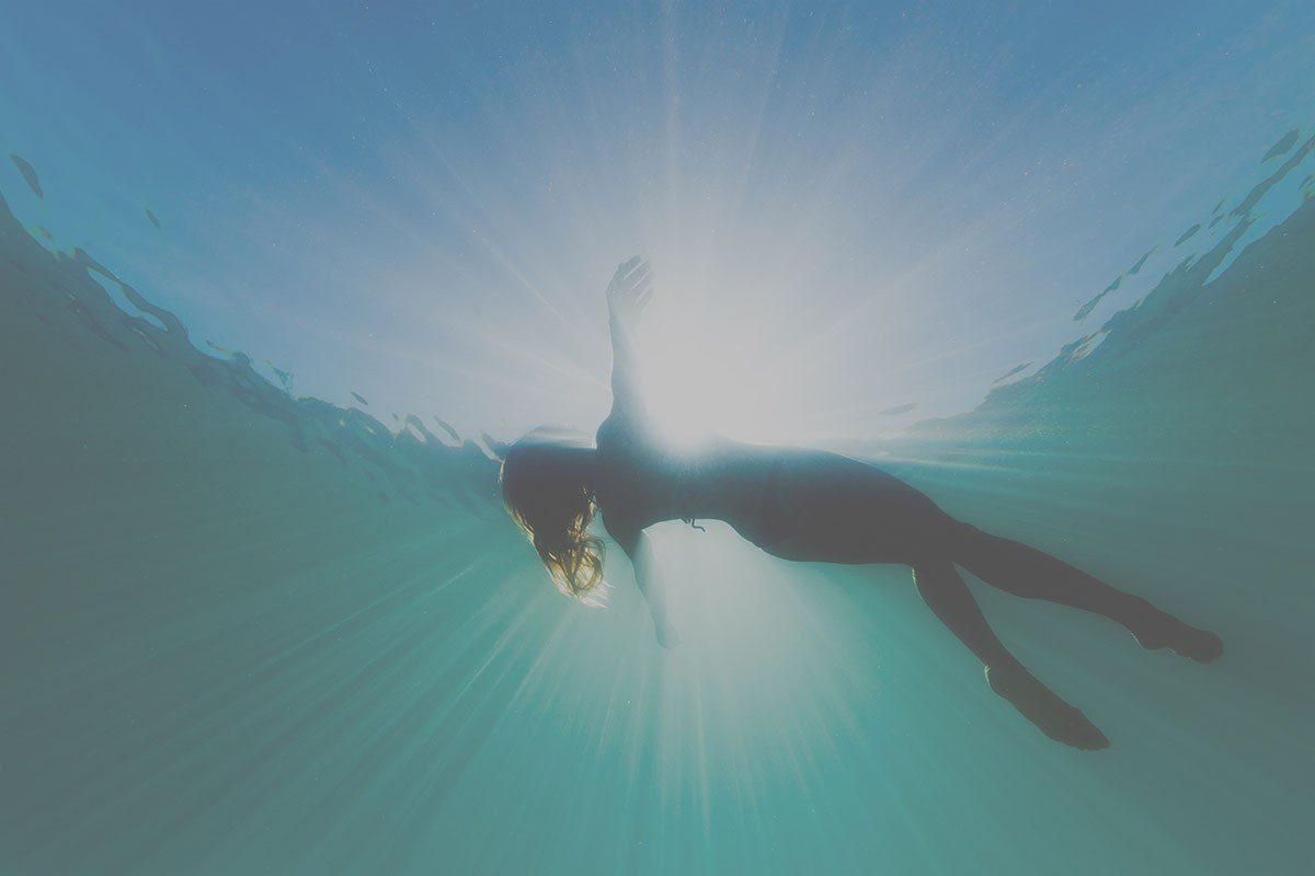 Background banner of a woman floating in open water with lighting coming through the water.
