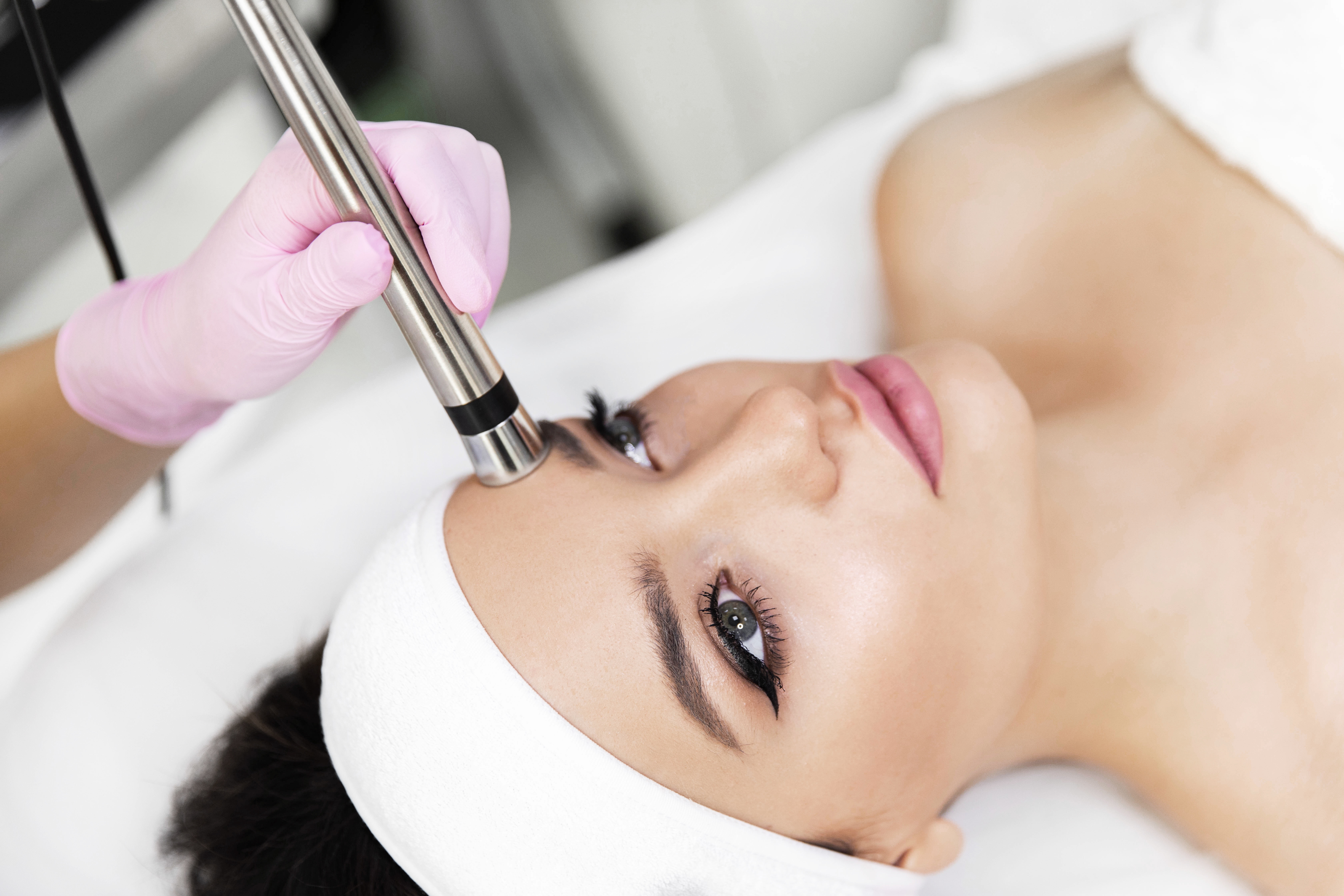 Woman with white headband receiving micodermabrasion from person wearing a pink glove.