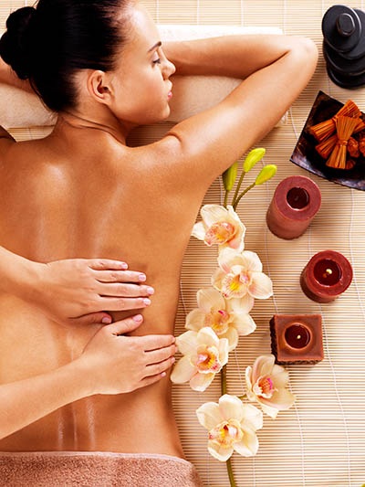 Woman getting a massage while laying on the floor next to candles and flowers.